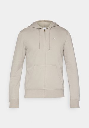 Bézs színű cipzáros pulóver puha anyagból, elülső zsebfedéllel, állítható húzózsinórokkal, bordázott mandzsettákkal és egy kis logóval a mellkason.