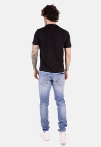 Camisa negra de manga corta, vaqueros ajustados azules, zapatillas blancas. La camisa tiene una textura suave; los vaqueros presentan bolsillos traseros y un acabado desgastado.