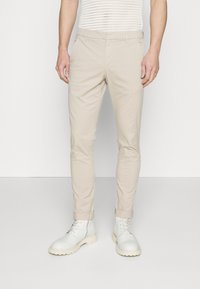 Pantalons chinos beiges à coupe slim, avec des revers roulés et une texture lisse. Associés à des bottes blanches à lacets.