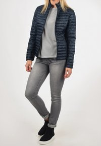 Granatowa pikowana kurtka z stójką, szary paskowany top, szare dżinsy i czarne buty wsuwane na białej podeszwie.