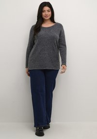 Grijze, lange mouwen trui met een ronde halslijn en een zachte textuur, gecombineerd met donkerblauwe, wijde jeans en zwarte schoenen.