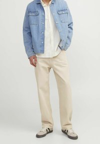 Světle modrá denimová bunda, bílá pruhovaná košile, krémové kalhoty a šedé tenisky s černými akcenty. Mezi rysy patří kapsy a knoflíkové zapínání.