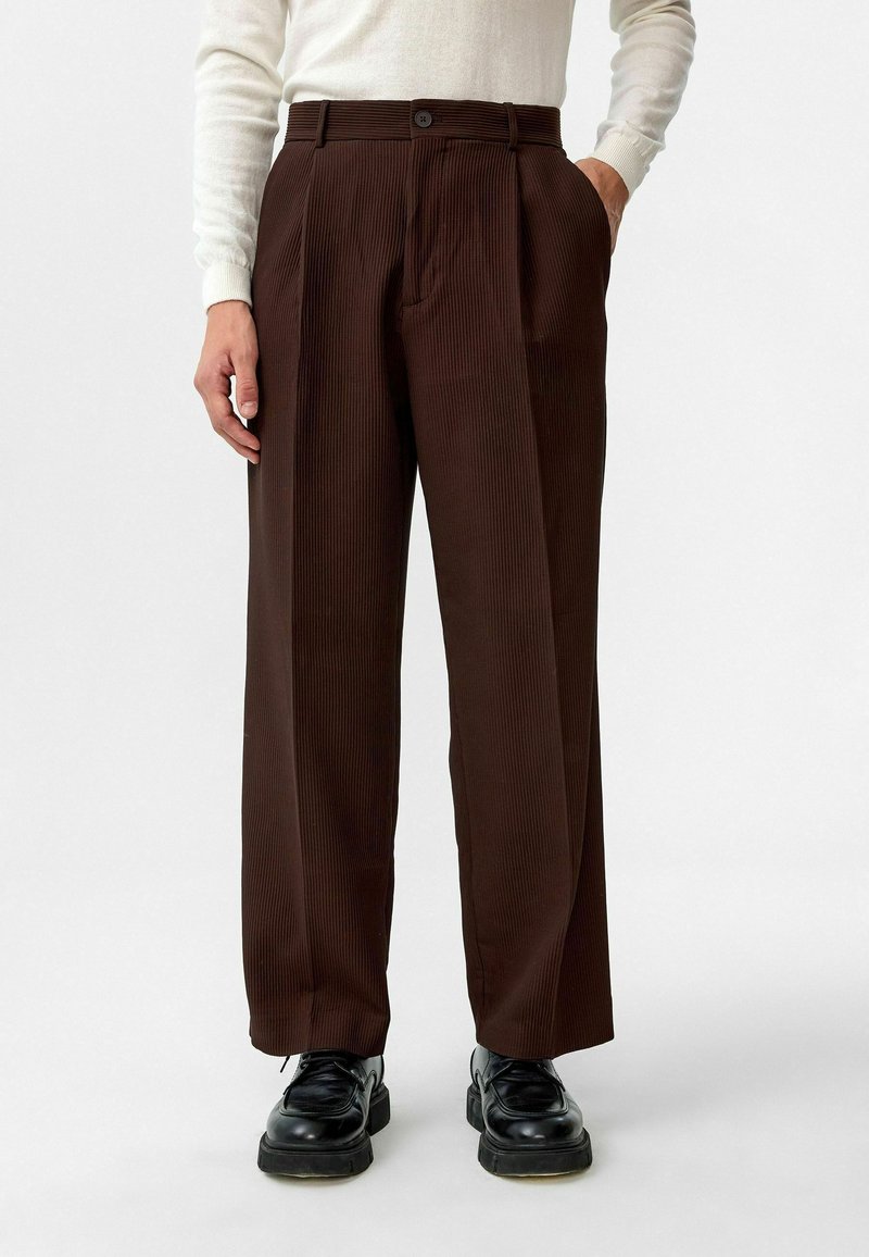 Bruine geribbelde broek met een hoge taille, voorzien van twee zijzakken, een knoopsluiting en een ontspannen, wijde pasvorm. Textuurafwerking van de stof.