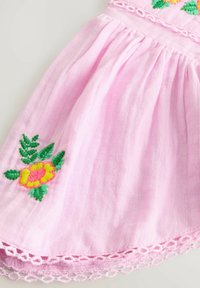 Pink fabric with green and yellow embroidered flowers and lace trim along the edge, showing texture and decorative stitching.