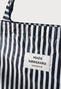 Tote bag i stoff med vertikale svarte og lyseblå striper, med en rektangulær hvit etikett som viser "MADS NØRGAARD COPENHAGEN."