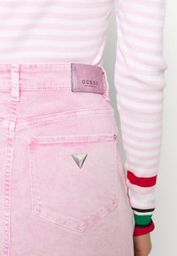 Roze denimrok met een Guess-logo patch, met een driehoekige metalen accent op de achterzak en een hoge taille.