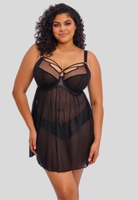 Musta läpikuultava yömekko, jossa on muotoiltu yläosa, säädettävät olkaimet ja koristeelliset hihnakiinnitykset. Valuu pehmeästi puoliväliin reittä.