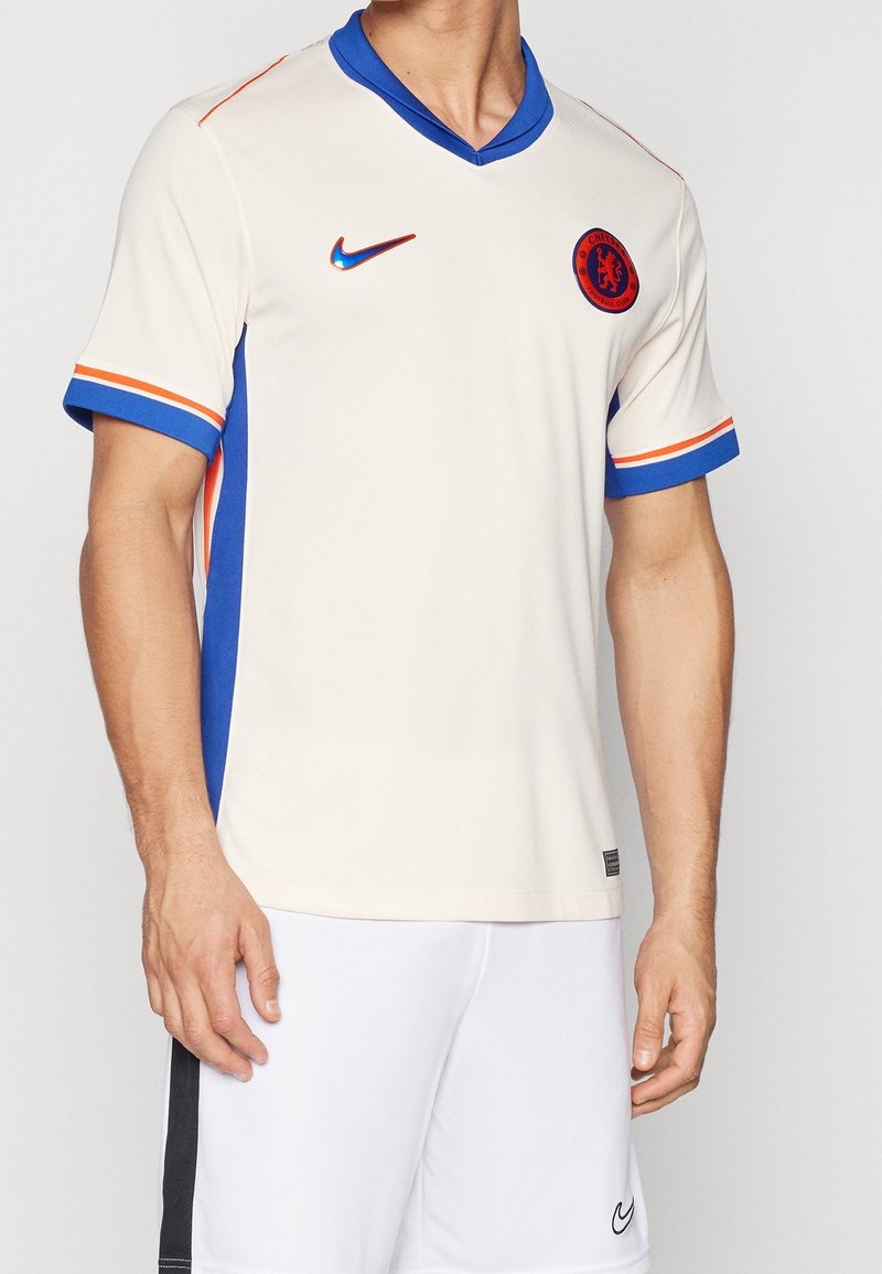 Das Trikot des Chelsea Football Club in Creme mit blauen und orangefarbenen Akzenten, V-Ausschnitt-Design, kurzen Ärmeln, atmungsaktivem Stoff und Logo auf der Brust.