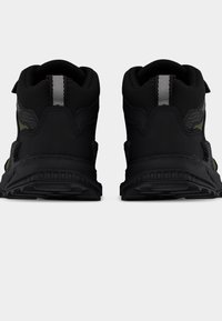 Baskets hautes noires en tissu texturé, avec un accent vert et un détail réfléchissant. Elles sont dotées d'une semelle en caoutchouc et d'un col coussiné.