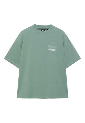 T-shirt oversize verde salvia a maniche corte con scollo rotondo e testo bianco "Stwd Playful Universe" sul petto a sinistra.