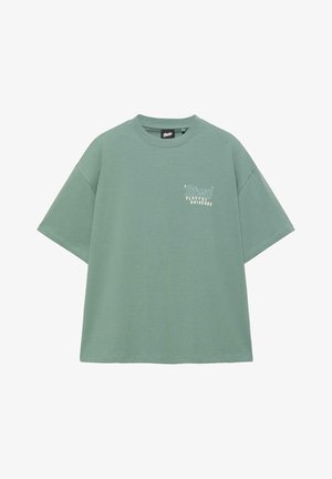 T-shirt oversize vert sauge à manches courtes avec col rond et texte blanc "Stwd Playful Universe" sur le côté gauche de la poitrine.