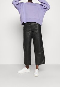 Sudadera corta de color púrpura claro, pantalones anchos de cuero negro y zapatillas blancas. Texturas elegantes y colores contrastantes.