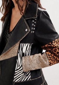 Giubbotto in pelle nera con stampe miste: zebra, leopardo e texture maculate. Borchie argentate evidenziano la spalla. Cuciture dettagliate.