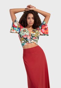 Květinový crop top v jasných barvách, s krátkými volnými rukávy a designem do zavinování. V kombinaci s dlouhou, hladkou červenou sukní.