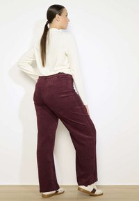 Pantaloni in corduroy bordeaux con vestibilità rilassata, dotati di un'alta vita e tasche laterali, abbinati a un top color crema.