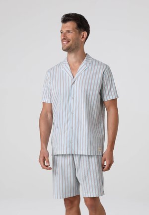 Uomo che indossa una camicia a righe a maniche corte con bottoni e pantaloncini abbinati, sorridente e che guarda di lato su uno sfondo uniforme.