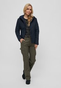 Jachetă cu glugă de culoare bleumarin, cu fermoar, cămașă cu model camuflat dedesubt și pantaloni cargo de culoare măslinie, cu buzunare laterale și croi lejer.