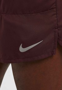 Maroonit urheilushortsit, jotka on valmistettu kevyestä kankaasta. Niissä on hopeinen Nike-logo, sileä pinta ja säädettävä vyötärö.