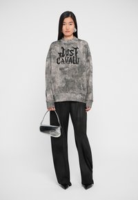 Cachecol cinza com texto preto, corte solto, combinado com calças largas pretas e uma pequena bolsa prateada com logótipo em relevo. Textura suave.