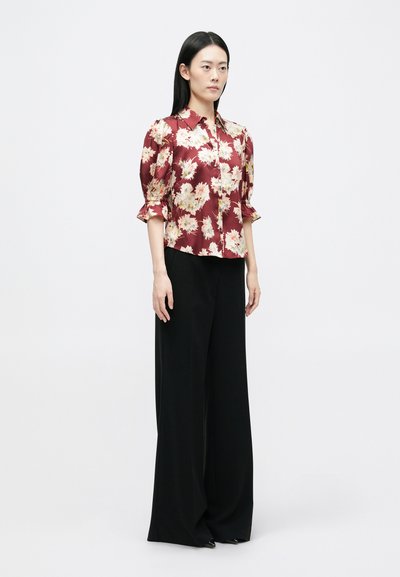 Burgundi virágmintás blúz rövid puffujjakkal, gombos kialakítással. Fekete, magas derékú, laza nadrággal párosítva. Sima textúra.