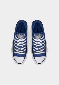 Μπλε αθλητικά παπούτσια Converse χαμηλής κορυφής με λευκές μύτες, κορδόνια και σχέδιο αστεριού, εμφανίζονται από πάνω σε λευκό φόντο.