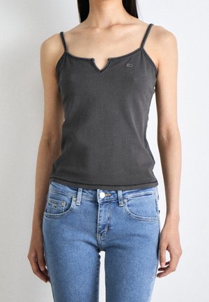 Woman wearing a dark gray ribbed tank top with a notch neckline and light blue jeans, standing against a plain white background.