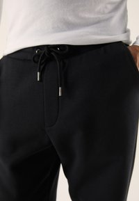 Mustad vabaaja dressipüksid, mis on valmistatud siledast kangast, varustatud elastse vöökohaga, millel on must nöör ja metallist otsad ning küljetaskud.