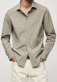 Chemise boutonnée gris clair en tissu doux, à manches longues, col pointu et coupe régulière, associée à un pantalon beige.
