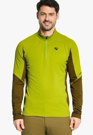 Uomo che indossa un top sportivo lime verde e marrone a maniche lunghe con zip, con loghi sul petto e sulla manica sinistra.
