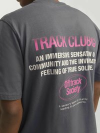 T-shirt en coton gris avec un texte audacieux en blanc et rose au dos. Le texte comprend "TRACK CLUB" et "Off Track Society" avec un accent circulaire.