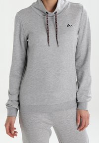 Sweat à capuche gris avec un col entonnoir, des cordons noirs et un petit logo. Tissu doux, manches longues et poignets ajustés.