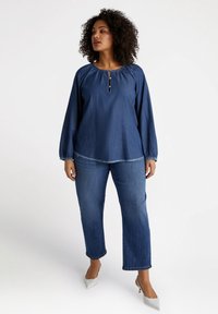 Top in denim con maniche lunghe, collo tondo e dettagli con bottoni. Abbinato a pantaloni in denim azzurro e décolleté grigio chiaro a punta.