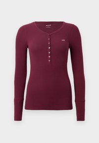 Bordo dugodlaki henley majica s okruglim izrezom, rebrastom teksturom i šest dugmadi sprijeda. Mali logo na prsima.