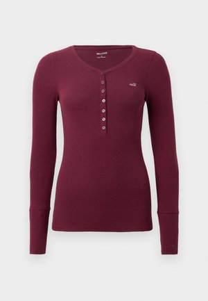 Bordo dugodlaki henley majica s okruglim izrezom, rebrastom teksturom i šest dugmadi sprijeda. Mali logo na prsima.