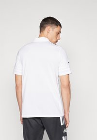Polo shirt blanc avec un col classique, manches courtes et ourlet droit, associé à un pantalon de sport noir avec trois bandes blanches.