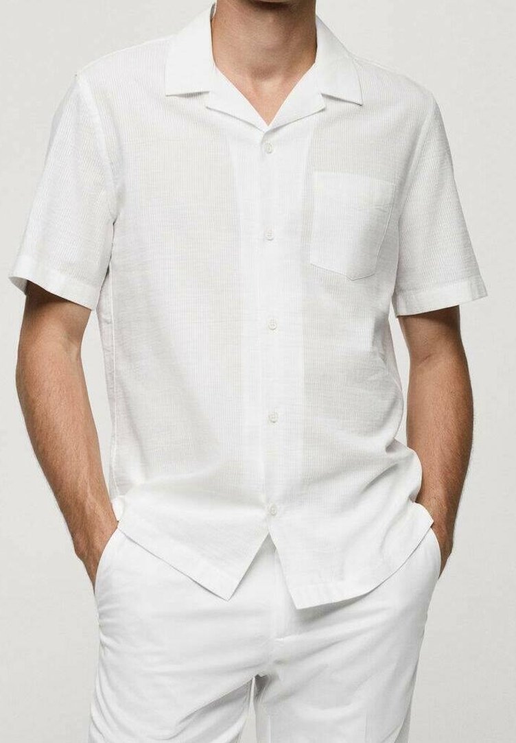 Camicia bianca a maniche corte con un sottile motivo a quadri, chiusura a bottoni e taschino sul petto. Realizzata in tessuto leggero, adatta per il clima caldo.