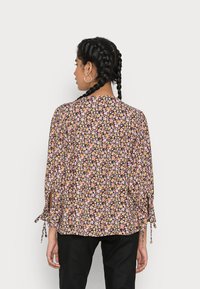 Blusa floral com fundo preto, apresentando flores em rosa, amarelo e branco. Tem detalhes de laço nas mangas e um design solto.