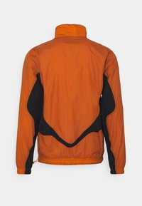 Orange och svart lättviktsjacka sedd bakifrån med långa ärmar, hög krage och elastisk midja.