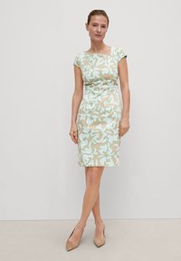 Beiges Kleid mit hellblauem Blumenmuster, figurbetontem Design, kurzen Ärmeln, knielang, kombiniert mit nudefarbenen Schuhen.