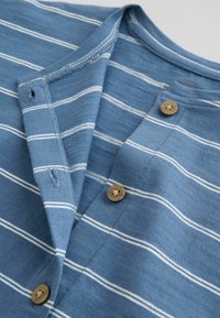 Maglietta di maglia blu con strisce orizzontali bianche, dotata di bottoni di legno e asole lungo l'apertura frontale.