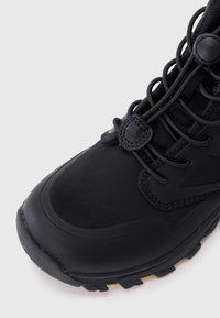 Scarpa da trekking nera con tomaia in sintetico liscio, lacci testurizzati e suola robusta con accenti gialli per una trazione migliorata.