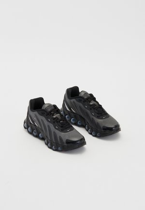 Paire de baskets noires et gris foncé avec semelles à coussin d'air brillantes et design à lacets sur fond blanc.