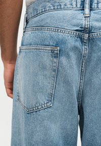 Háttal álló személy világoskék farmernadrágban, a hátsó zseb és a derékrész kiemelve.