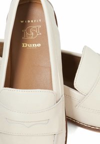 Wide-fit loafers made of cream leather with a smooth texture, featuring a stitched seam and a subtle decorative design on the front.
