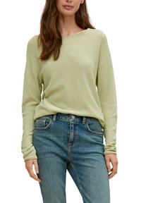 Jasnozielony sweter z długim rękawem o teksturowanym wzorze, z okrągłym dekoltem i luźnym krojem, w zestawieniu z niebieskimi dżinsami.