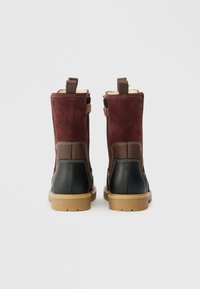 Par van laarzen tot halverwege de kuit met een bordeauxrode suède bovenkant, bruine leren enkeldetails, zwarte hak, beige zool en achterkant met trekbanden op een witte achtergrond.