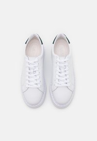 Zapatillas bajas blancas con cordones blancos y tiradores traseros verde oscuro, vistas desde arriba sobre un fondo blanco liso.