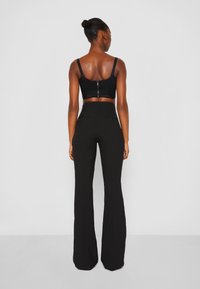 Top noir court avec des bretelles spaghetti et une fermeture éclair dans le dos, associé à un pantalon évasé noir taille haute avec poches arrière.