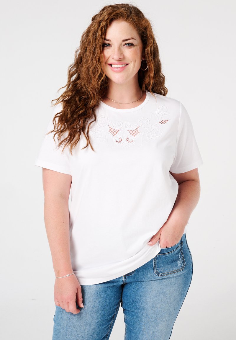 Witte T-shirt met korte mouwen, voorzien van geborduurde bloemmotieven rond de halslijn, gecombineerd met lichtblauwe spijkerbroek. Casual fit en zachte textuur.