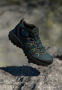Turkusowe buty trekkingowe z czarnymi akcentami; oddychająca siateczka górna, wyściełany kołnierz, odblaski i agresywna gumowa podeszwa zapewniająca przyczepność.